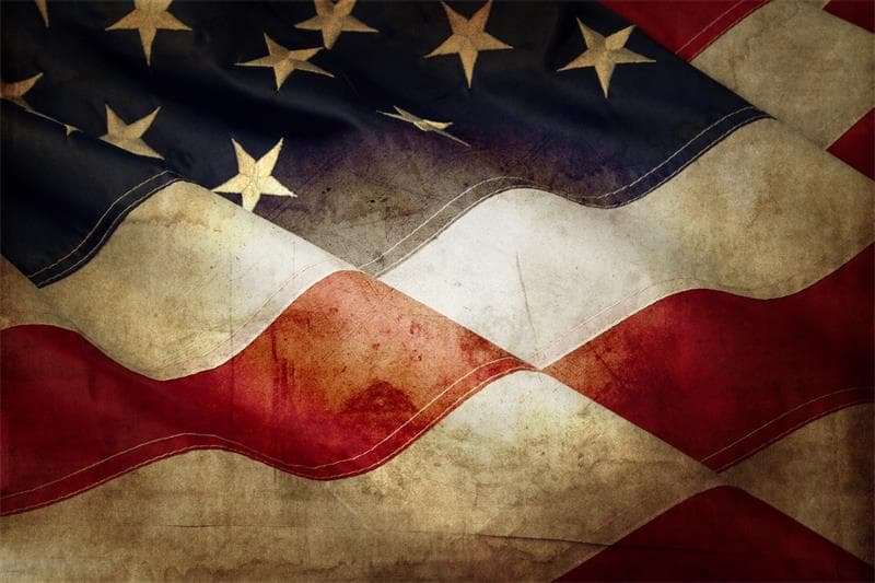 Close-up of a weathered, distressed American flag with wavy folds and an aged, vintage texture.